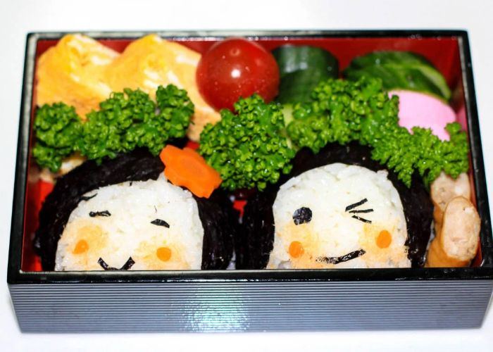 A onigiri-filled bento box, The rice balls are decorated with smiling faces.
